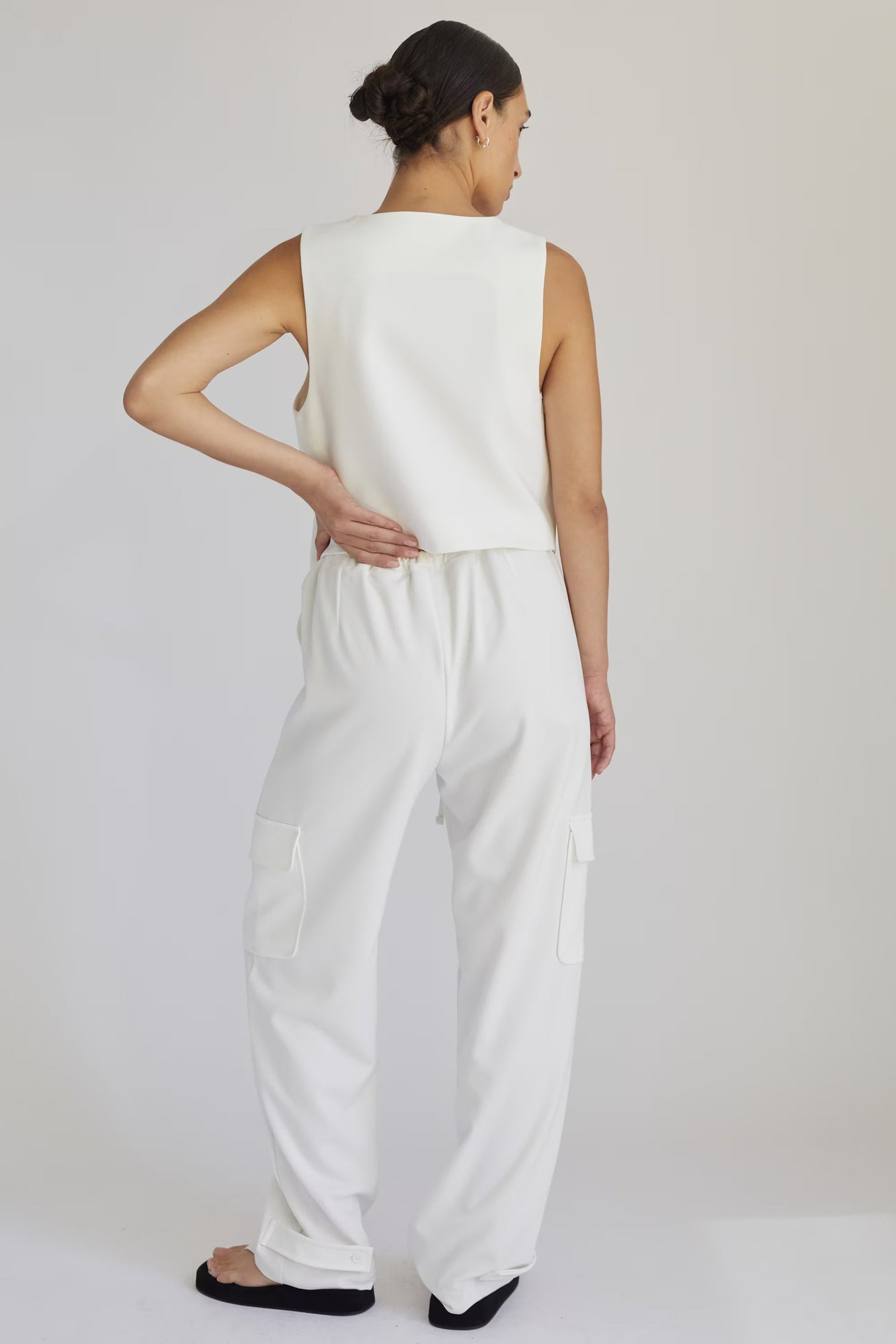 Woman wearing a white sleeveless top and pants on a plain background