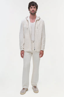 Man wearing cream zip-up hoodie jacket over white ribbed shirt, paired with cream pants and suede sneakers.