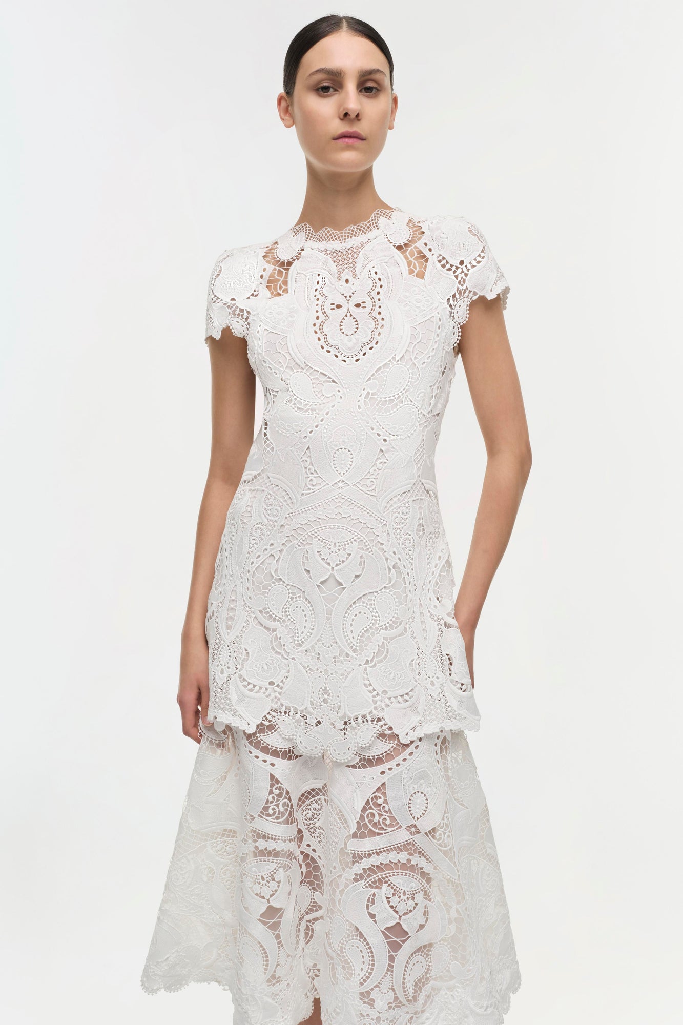 White lace dress with short sleeves, ornate cutout patterns throughout, and tiered ruffle hem.
