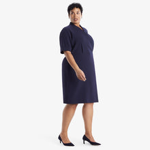 Side image of a woman standing wearing theTory Dress in dark iris