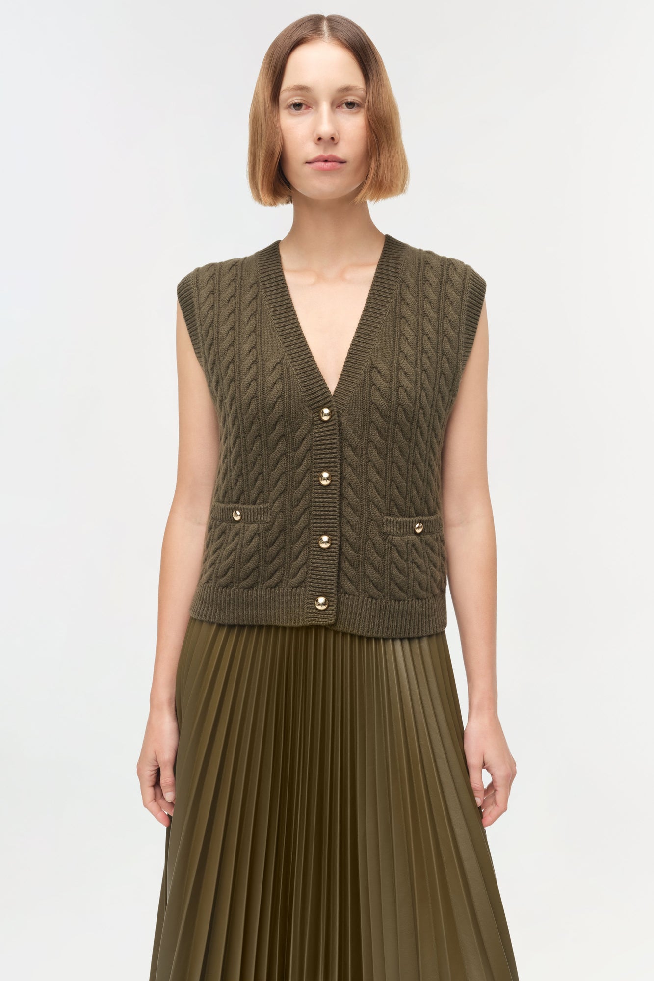 Olive green sleeveless cashmere vest with cable knit pattern, button front, and patch pockets.