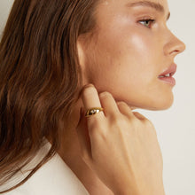 Model. Close-up of a woman wearing a gold earring on a plain background