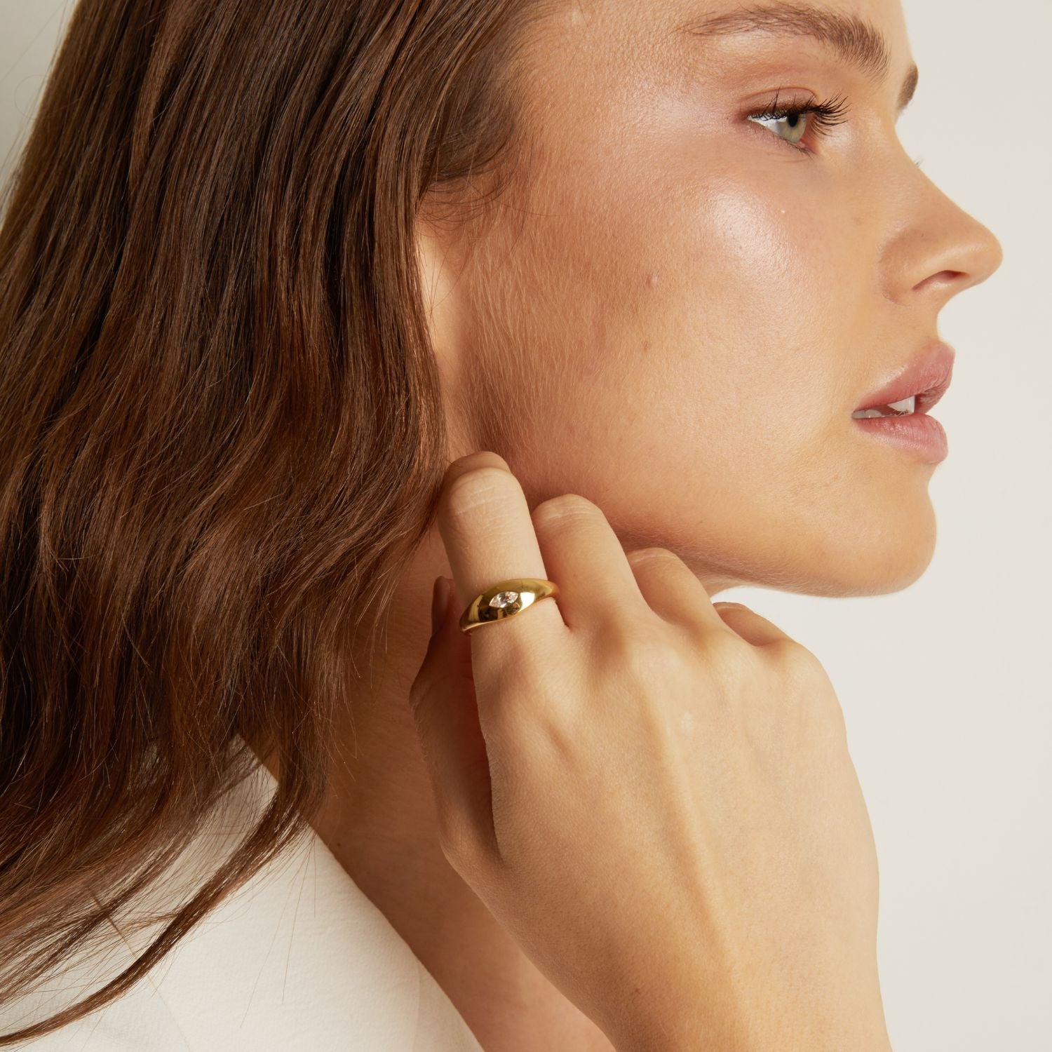 Close-up of a woman wearing a gold earring on a plain background