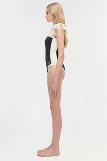 Woman wearing a black and white colorblocked one-piece swimsuit with halter neckline, shown from the side.