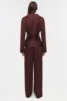 Woman wearing burgundy draped satin top with ruched waist detail and matching wide-leg pants, shown from back.