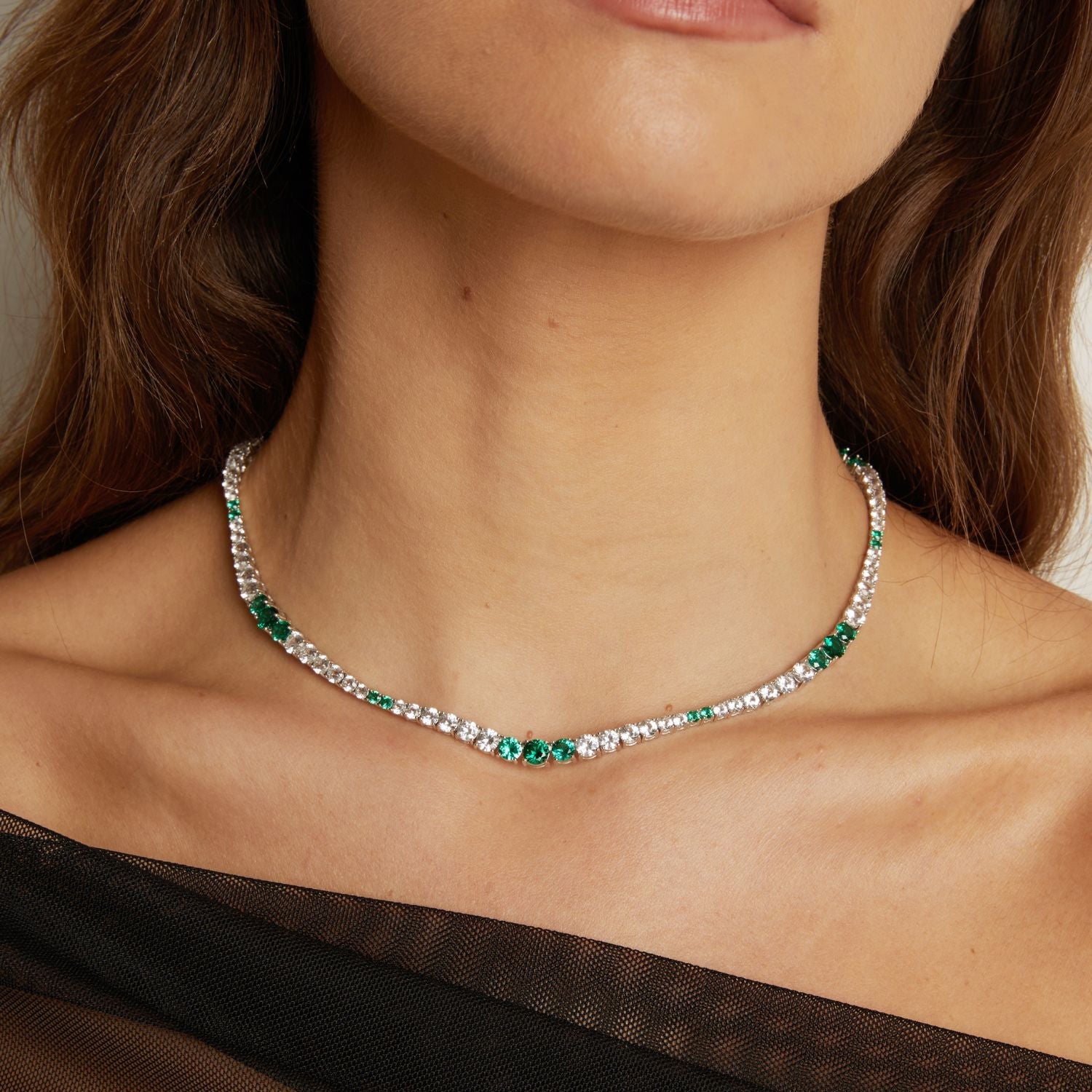 Model. Close-up of a woman wearing a silver necklace with green gemstones.