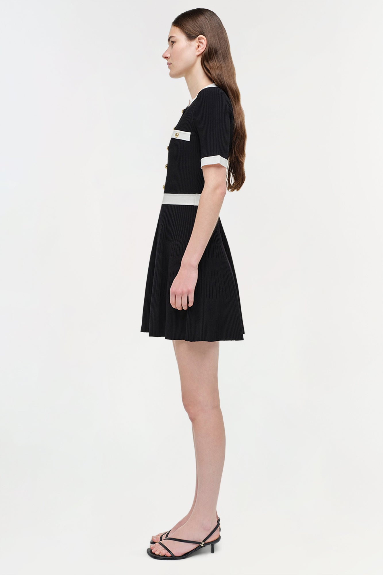 Black ribbed knit mini dress with white trim at neckline and waist, short sleeves, and pleated skirt.