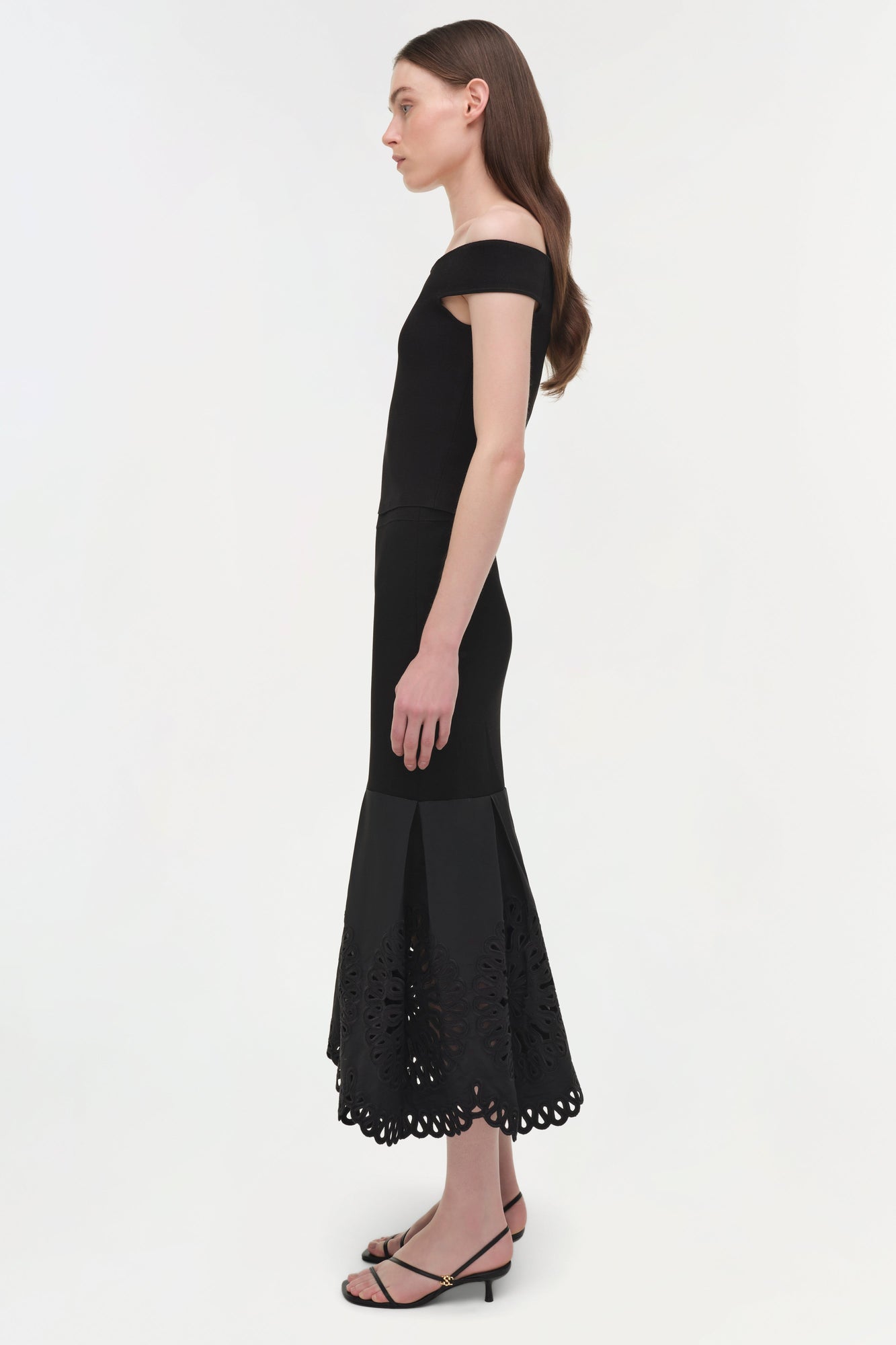 Woman wearing black off-shoulder knit midi dress with embroidered lace hem detail.