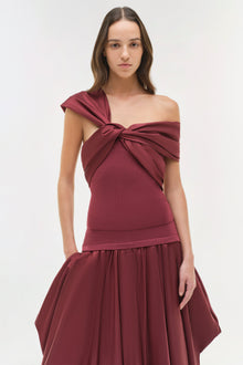Woman wearing a burgundy off-shoulder top with a twisted neckline and draped skirt detail.