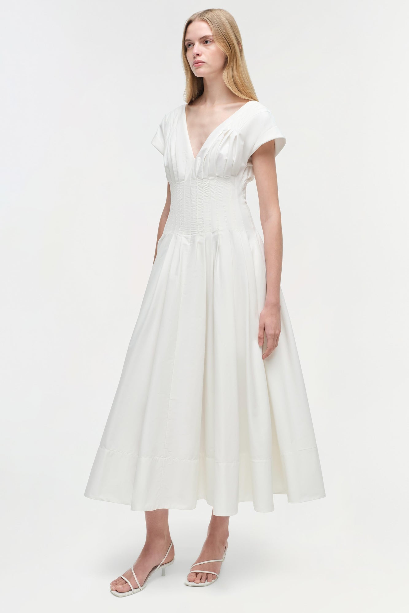 Woman wearing white cotton midi dress with short sleeves, V-neckline, and fitted waist with full skirt.