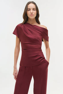 Burgundy draped satin top with asymmetrical off-shoulder neckline and short sleeves on model.