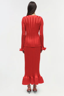 Red ribbed knit top with long sleeves, ruched cuffs, and fitted silhouette worn with matching midi skirt.