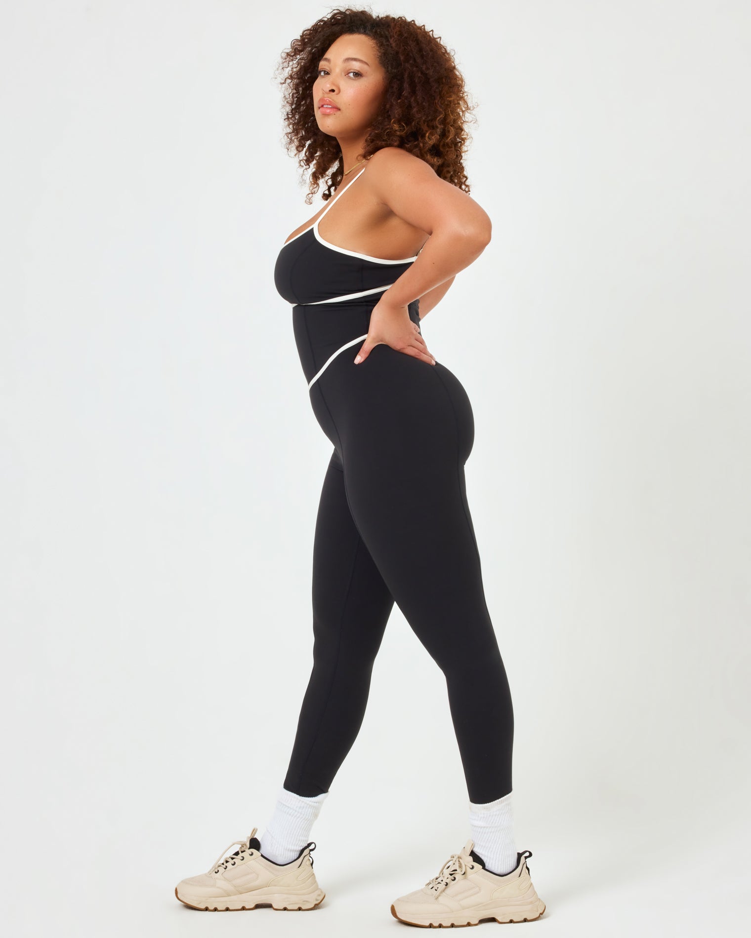 Side view of plus size model wearing the Ace Jumpsuit in black-cream showing the side cutout and cream contrast piping.