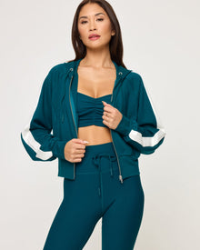 Close-up front view of model wearing the Back To Back Jacket in deep teal-cream, a zip-up track jacket with cream contrast panels and side stripe.