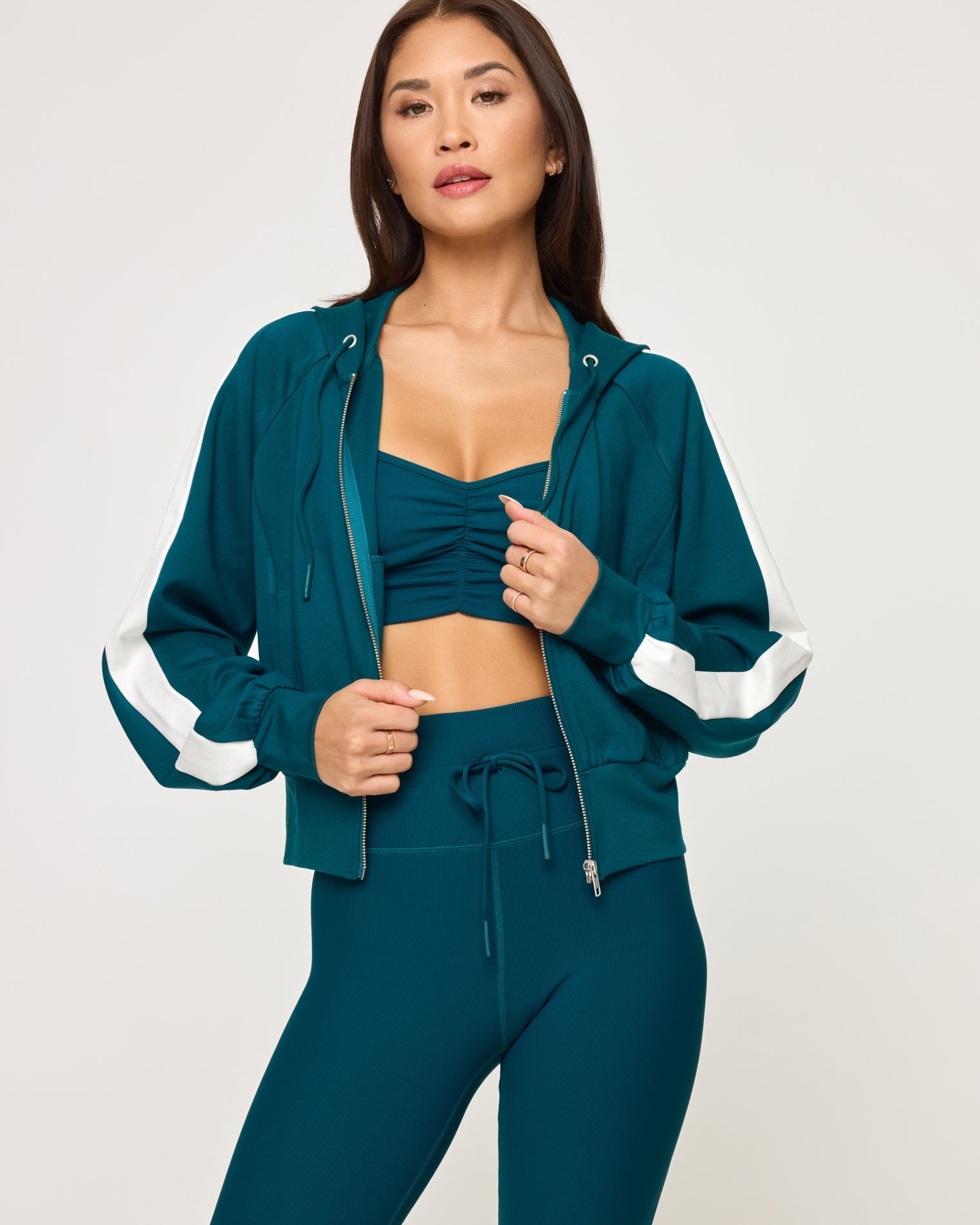 Close-up front view of model wearing the Back To Back Jacket in deep teal-cream, a zip-up track jacket with cream contrast panels and side stripe.