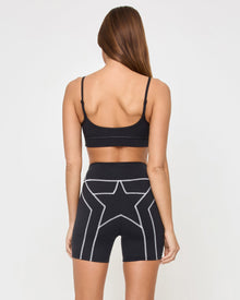 Back view of the LSPACE Star Power Shorts in black on a model against a white background, showing the white star and lightning bolt graphic on the seat of the bike shorts, paired with the matching black Eclipse Bra.