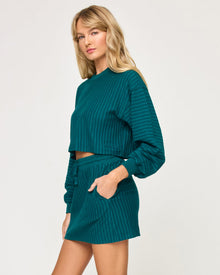 Side view of model wearing the Half Court Skirt in deep teal with matching deep teal Half Court Pullover, hand in pocket.