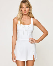 Close-up front studio view of model wearing the Ringside Dress in white showing the square neckline with lace-up detail and side slit at hem, hand on hip.