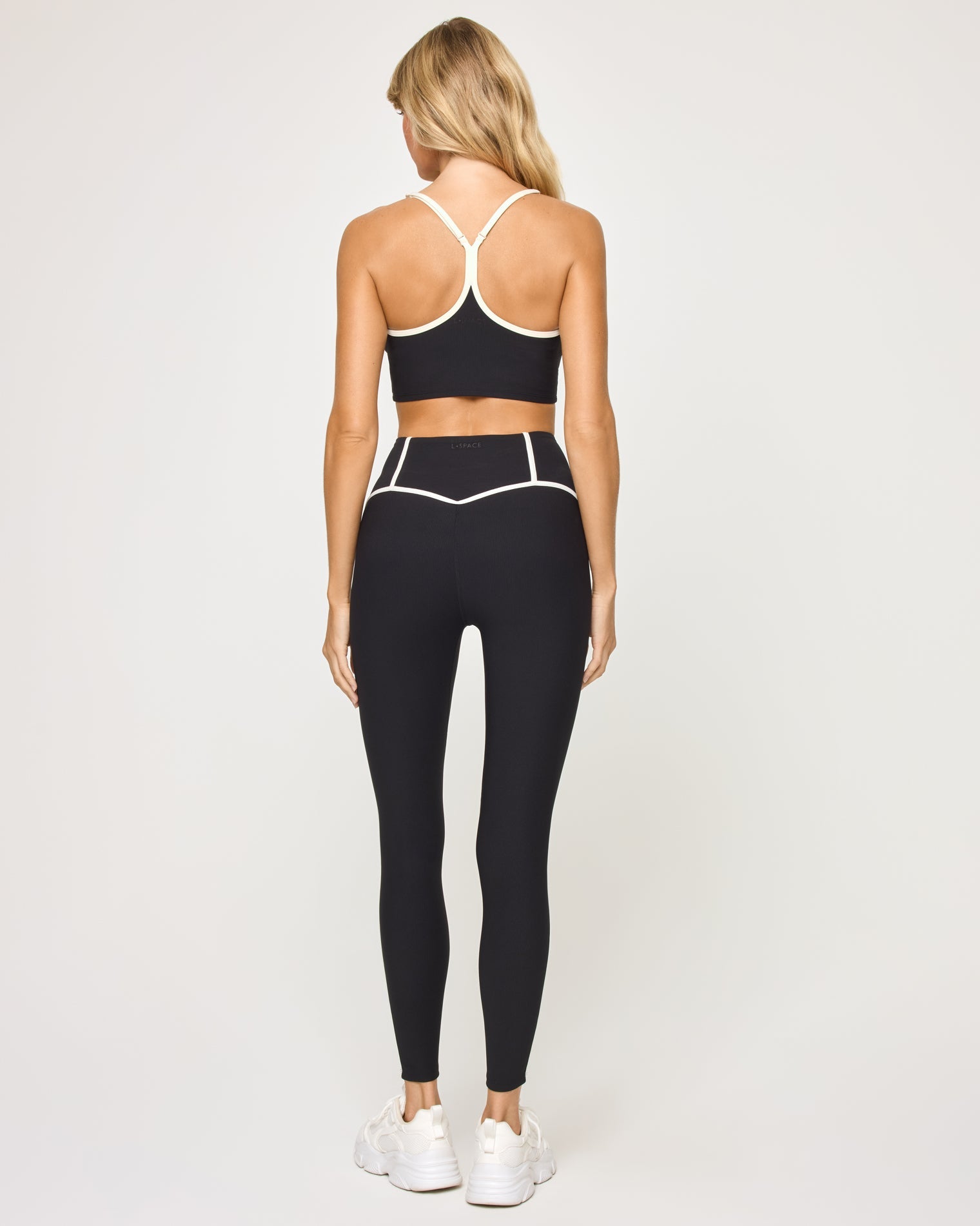 Back view of model wearing the Revel Legging in black-cream showing the cream piping on the waistband, with matching bra showing crossback detail.