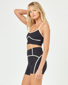 Side view of model wearing the Revel Short in black-cream showing the high-waist design and cream piping detail, with matching Revel Top.