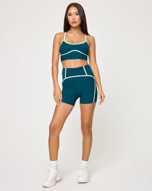 Front view of model wearing the Revel Top in deep teal-cream with matching deep teal-cream Revel Short, white socks and white sneakers.