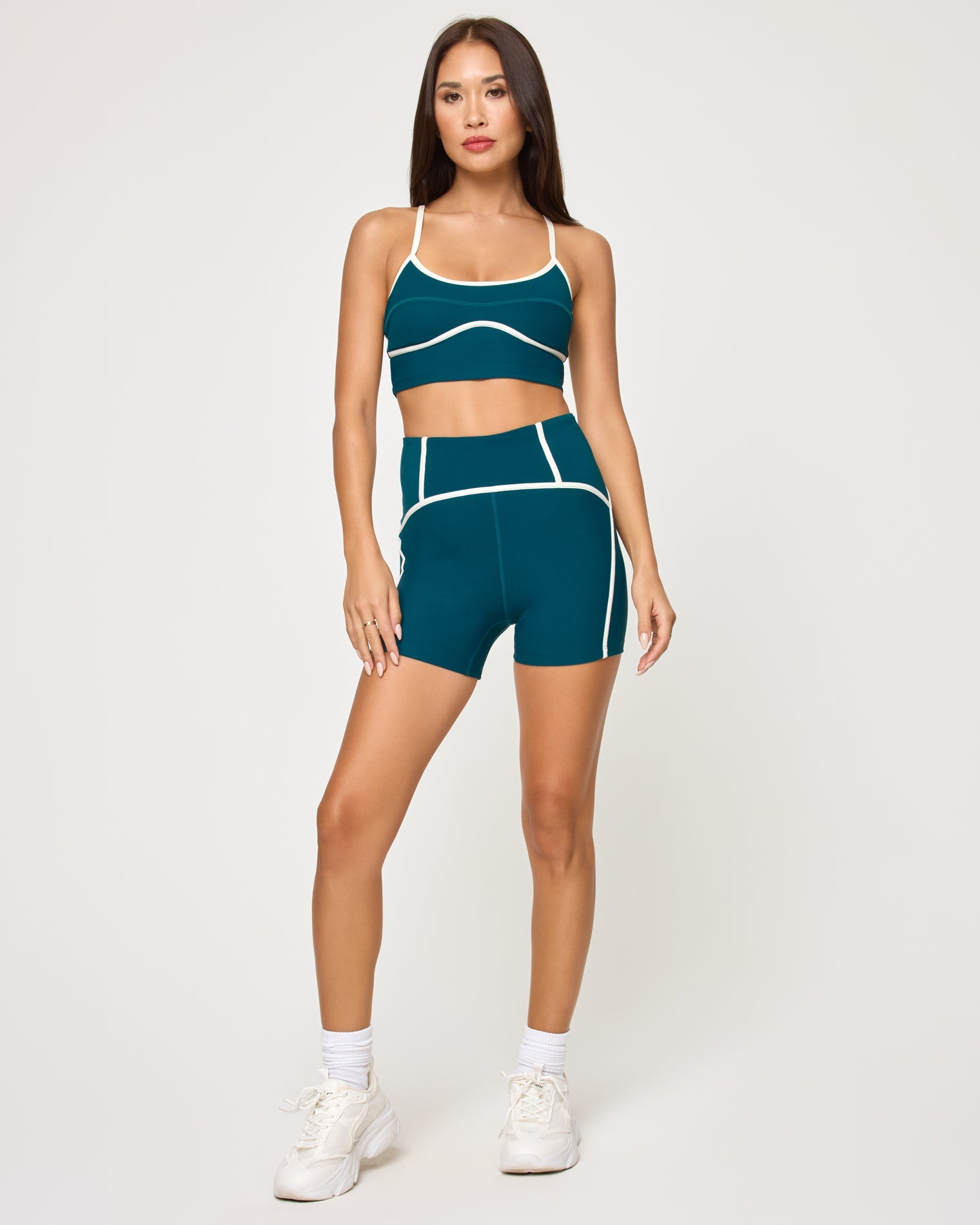 Front view of model wearing the Revel Top in deep teal-cream with matching deep teal-cream Revel Short, white socks and white sneakers.