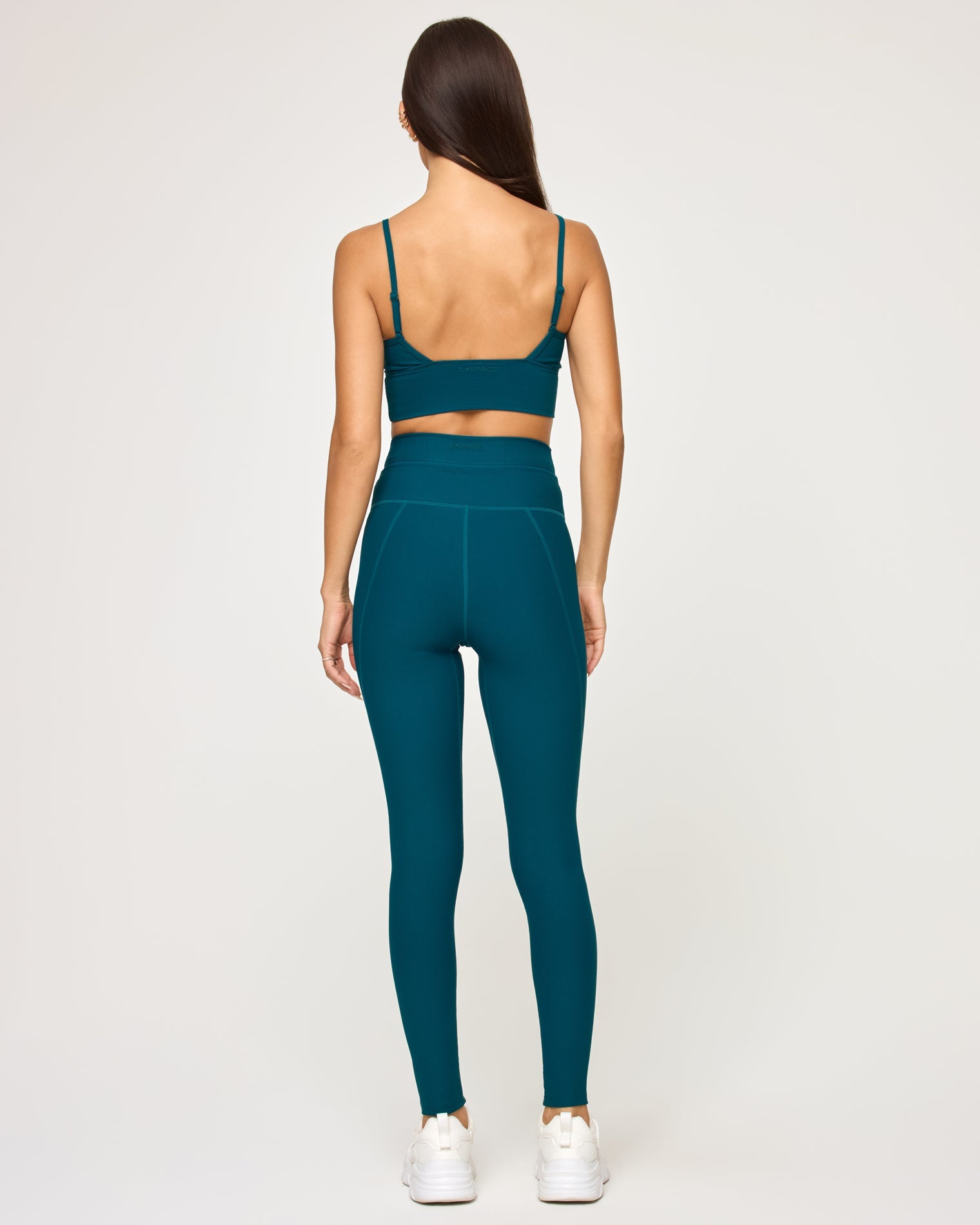 Back view of model wearing the Soren Top in deep teal showing the open crossback spaghetti strap detail, with matching deep teal Turner Legging and white sneakers.