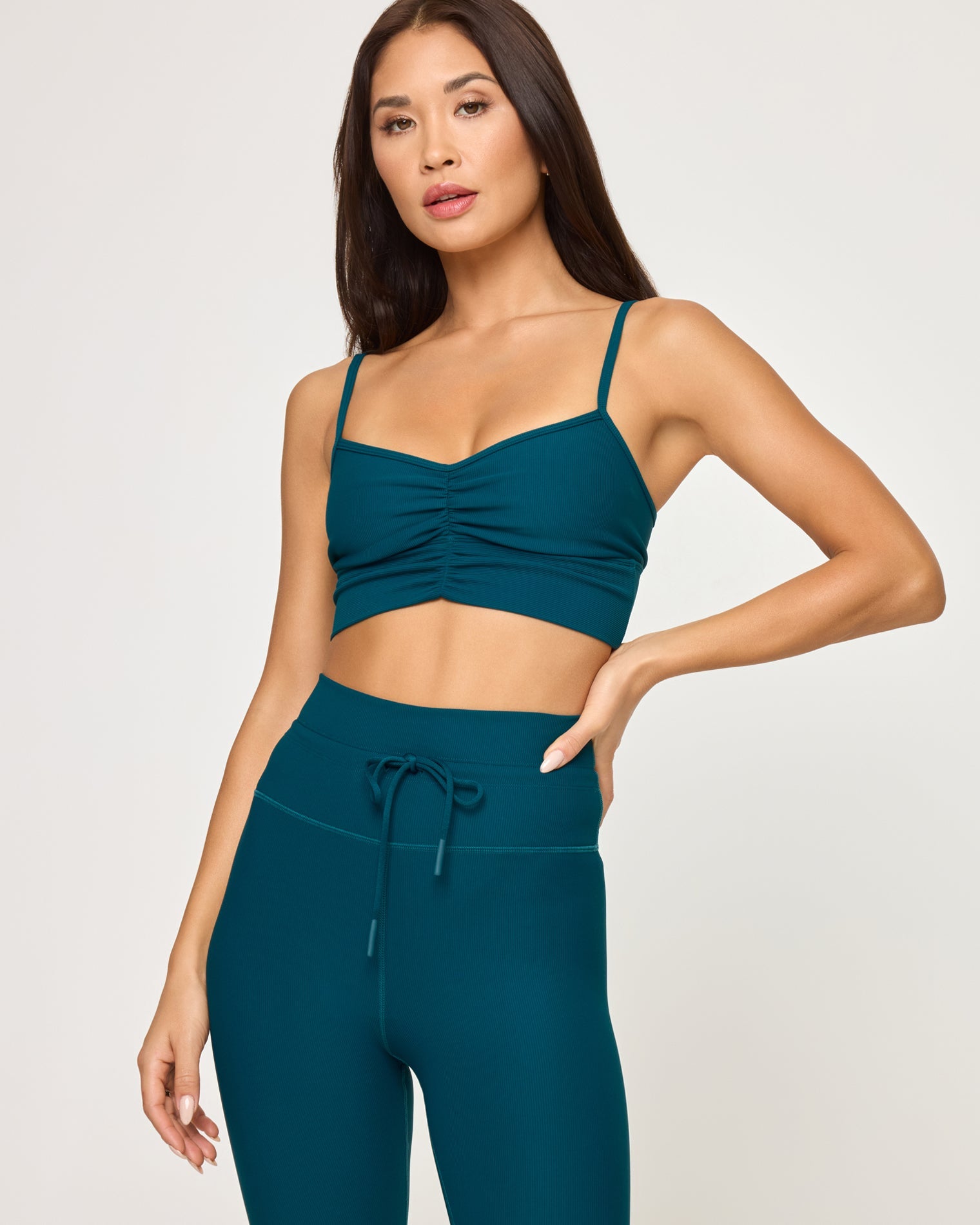 Close-up front view of model wearing the Soren Top in deep teal, a ruched sweetheart crop top with spaghetti straps, with matching deep teal Turner Legging with drawstring waist, hand on hip.