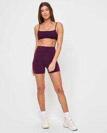 Front view of the LSPACE Stride Bra in plum on a model against a white background, showing the full plum sports bra design, paired with matching plum high-waist active shorts.