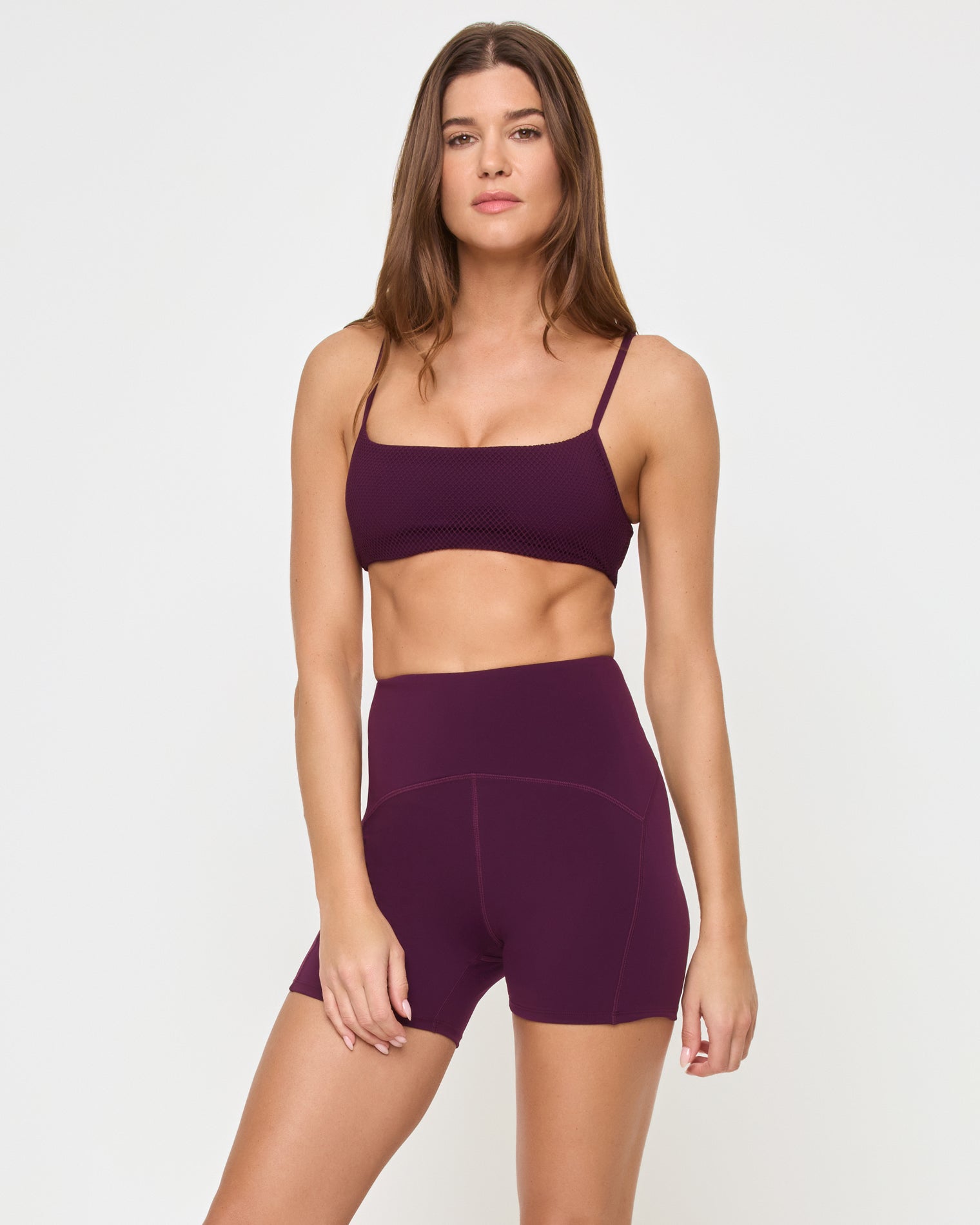 Front view of the LSPACE Stride Bra in plum on a model against a white background, paired with matching plum high-waist active shorts, showing the profile silhouette.