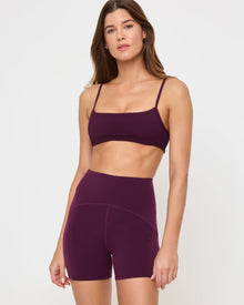 Close-up front view from the waist up of the LSPACE Stride Bra in plum on a model against a white background, showing the sports bra design, paired with matching plum high-waist active shorts.
