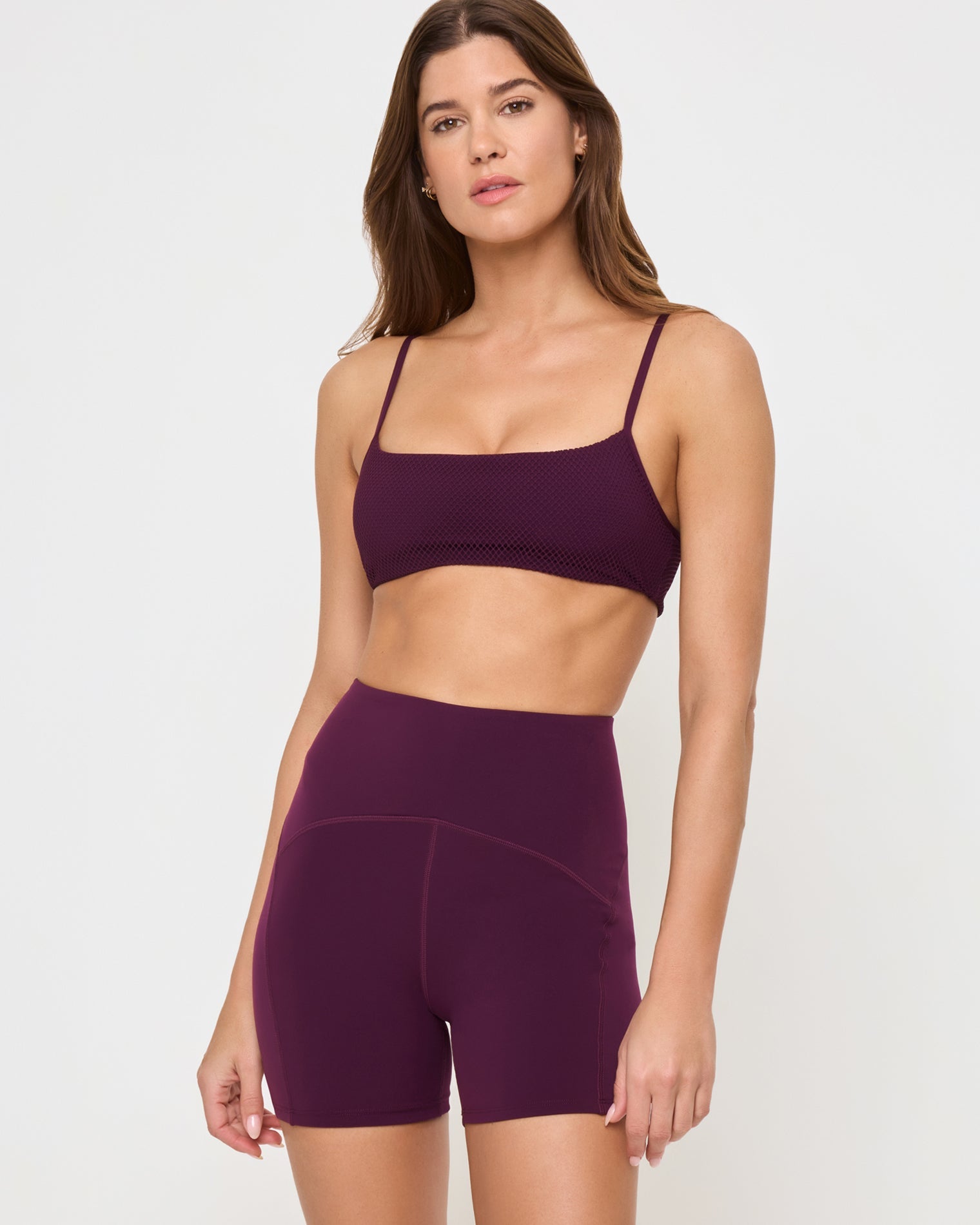 Close-up front view from the waist up of the LSPACE Stride Bra in plum on a model against a white background, showing the sports bra design, paired with matching plum high-waist active shorts.