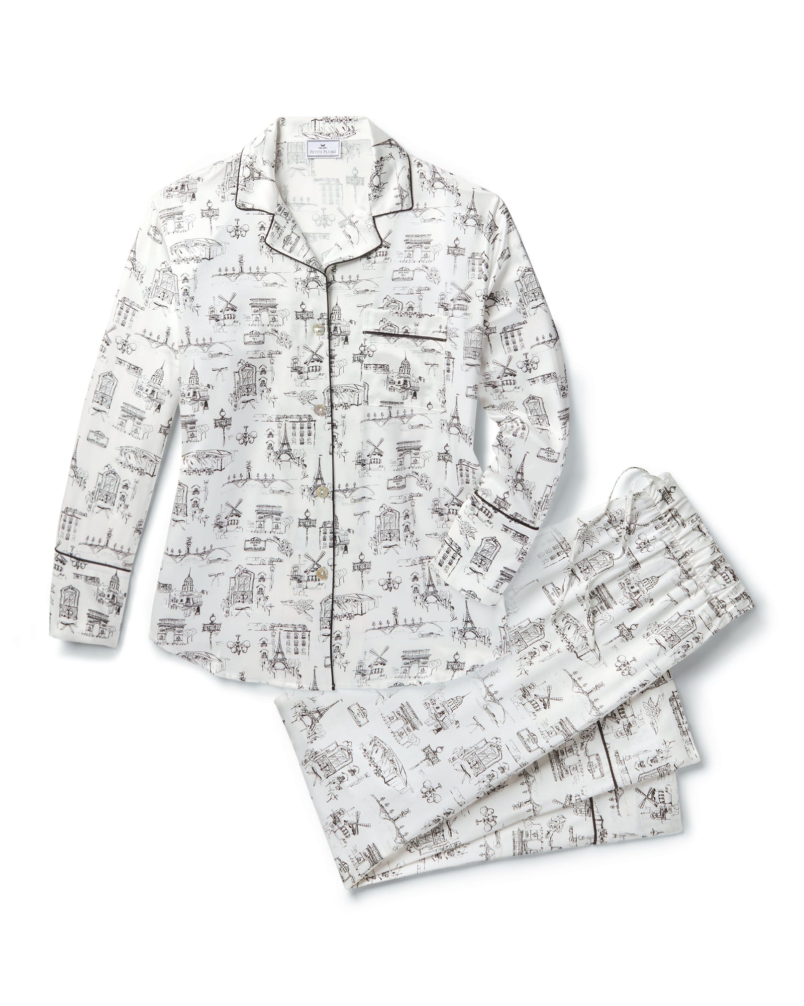 Women's Silk Pajama Set in Parisian Toile: white button-up with black piping, illustrated with buildings and trees. Includes long-sleeve top with chest pocket and matching long pants featuring an elastic waistband.