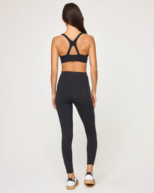 Back view of the LSPACE Uppercut Bra in black on a model against a white background, showing the crossback strap detail, paired with matching black high-rise active pants.