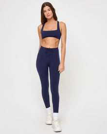 Front view of the LSPACE Contender Legging in midnight blue on a model against a white background, showing the full-length high-rise leggings with a corset-style lace-up front waistband detail, paired with the matching midnight blue square-neck sports bra.