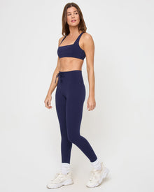 Side view of the LSPACE Contender Legging in midnight blue on a model against a white background, showing the lace-up side waistband detail, paired with the matching midnight blue square-neck sports bra.