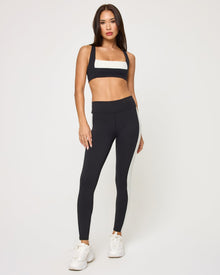Front view of the LSPACE Uppercut Bra in black-cream on a model against a white background, paired with black-cream high-rise active pants, showing the full-length outfit.