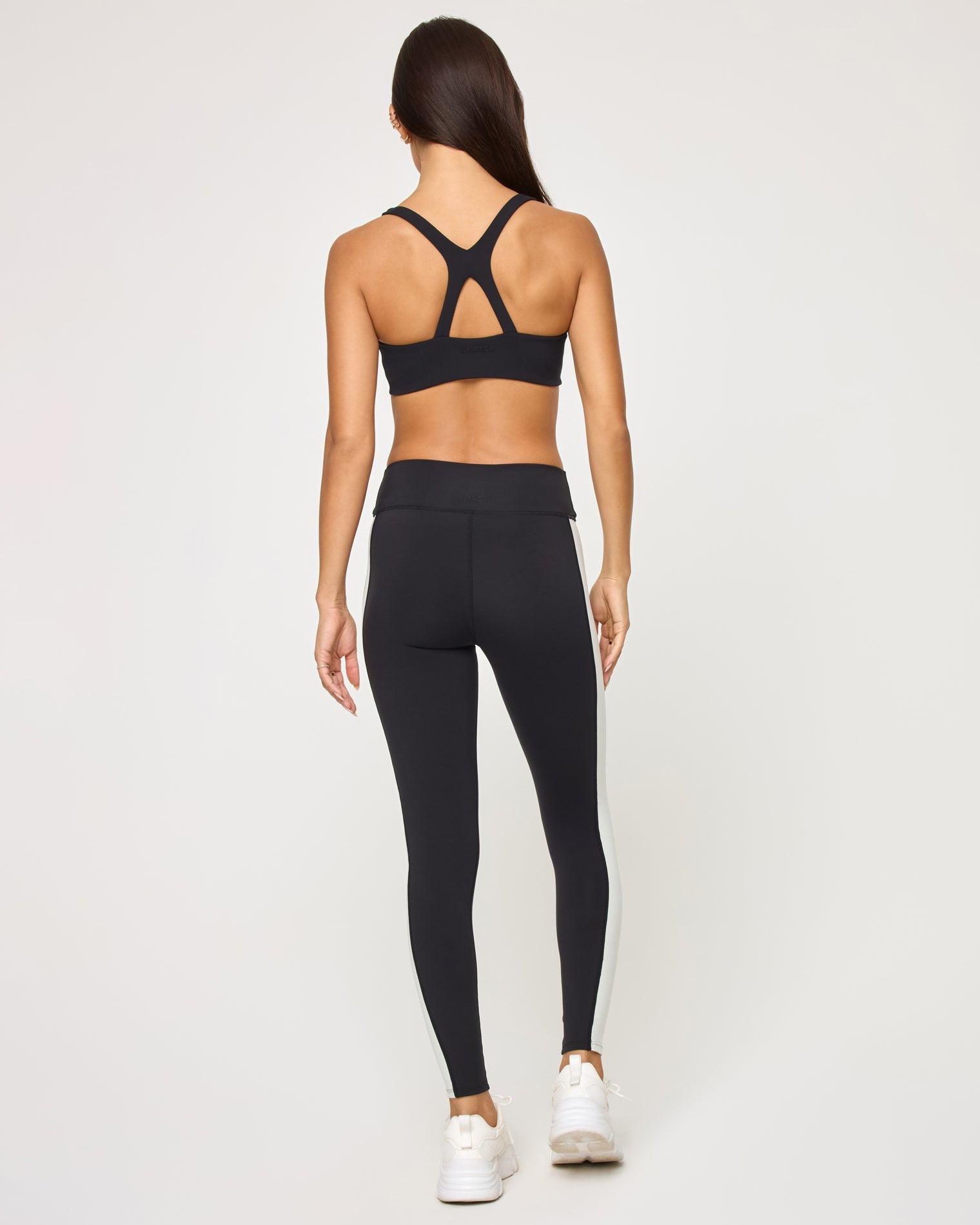Back view of the LSPACE Uppercut Bra in black-cream on a model against a white background, showing the crossback strap detail, paired with black-cream high-rise active pants.