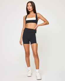 Front view of the LSPACE Uppercut Short in black-cream on a model against a white background, showing the high-rise active shorts with cream trim detail, paired with the matching black-cream Uppercut Bra.