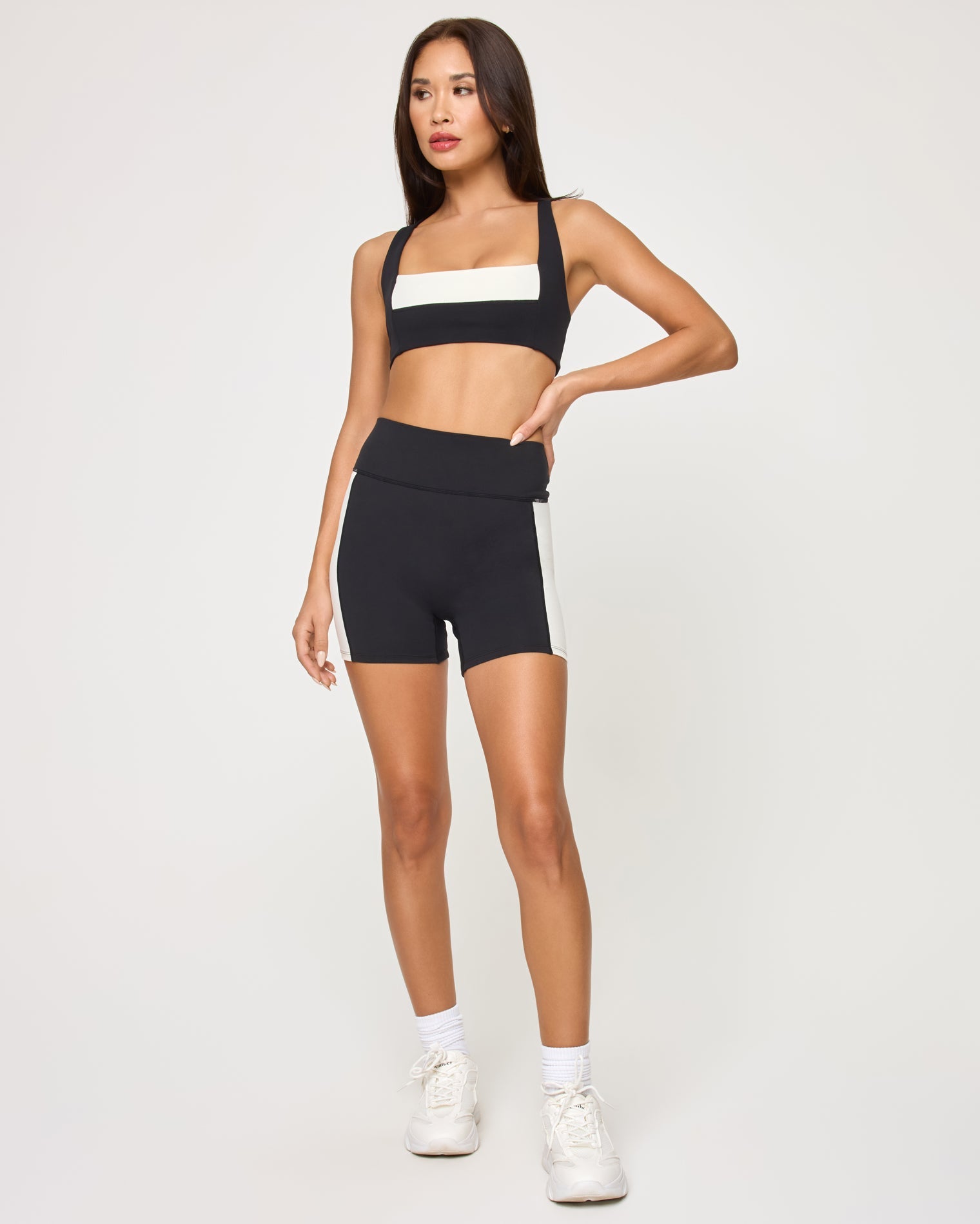 Front view of the LSPACE Uppercut Short in black-cream on a model against a white background, showing the high-rise active shorts with cream trim detail, paired with the matching black-cream Uppercut Bra.