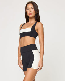 Side view of the LSPACE Uppercut Short in black-cream on a model against a white background, showing the profile of the high-rise active shorts, paired with the matching black-cream sports bra.