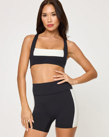 Close-up front view from the waist down of the LSPACE Uppercut Short in black-cream on a model against a white background, showing the high-rise waistband and cream trim detail of the active shorts.