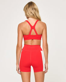 Back view of the LSPACE Uppercut Bra in flame-cream on a model against a white background, showing the crossback strap detail, paired with the matching flame-cream high-rise active shorts.