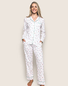 A person stands smiling, wearing the luxurious Womens Flannel Pajama Set in Apres Ski by Petite Plume. The top features green piping and a collar, while hands are in the pockets of loose-fitting, soft brushed cotton flannel pants. The background is a plain light color.