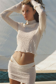 Woman wearing cream textured long-sleeve crop top with turtleneck and matching textured skirt.