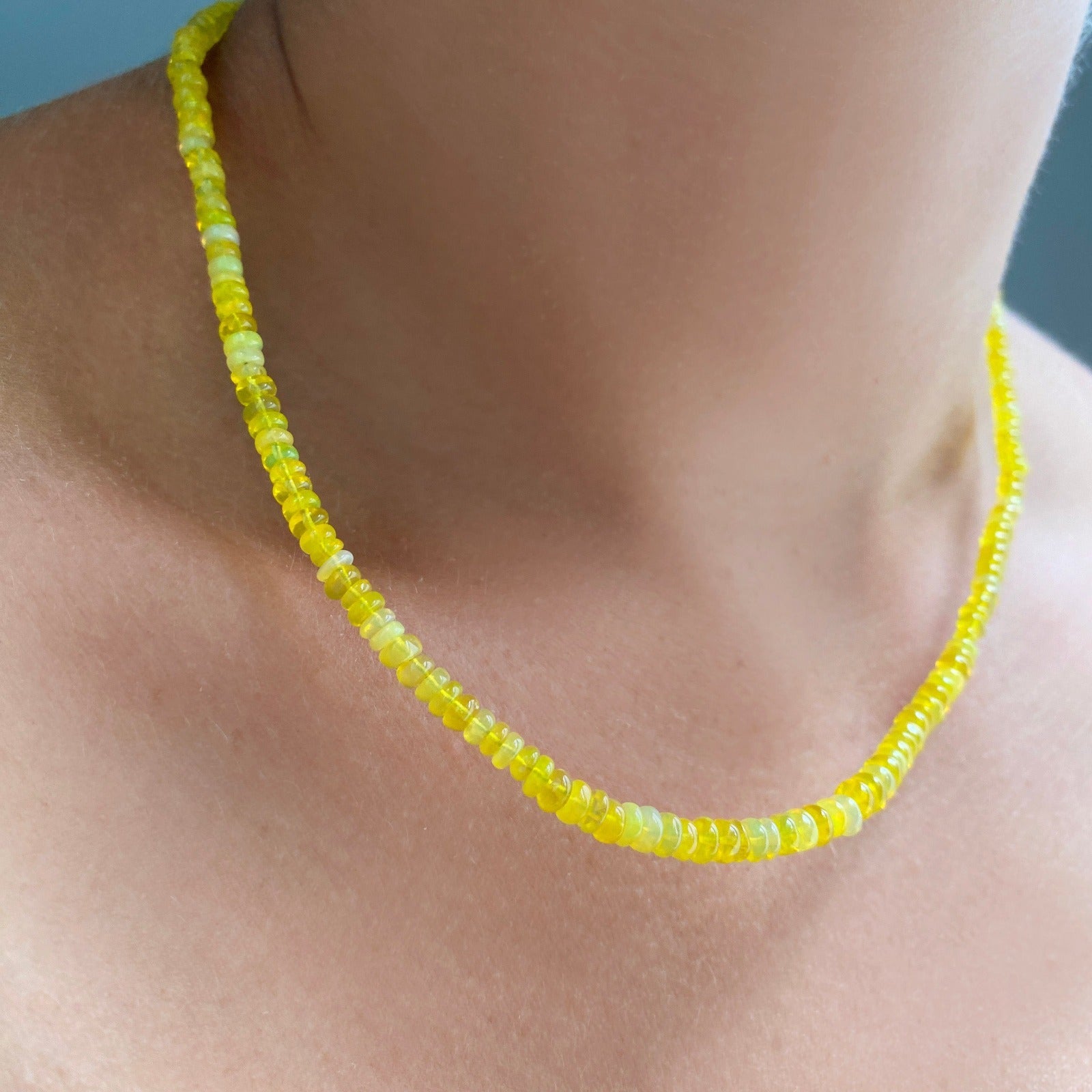 Shimmering beaded necklace made of smooth opals in shades of yellow on a gold linking ovals clasp
Styled on a neck