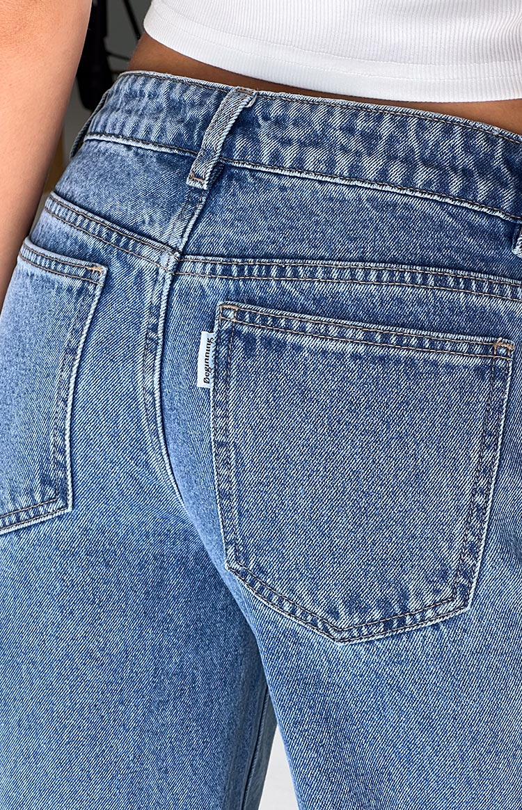 Close-up of the back right pocket of mid-wash denim jeans, showing the stitching, belt loops, and waistband