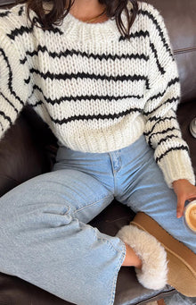 Rear view of a white and black striped chunky knit cropped sweater with long voluminous sleeves