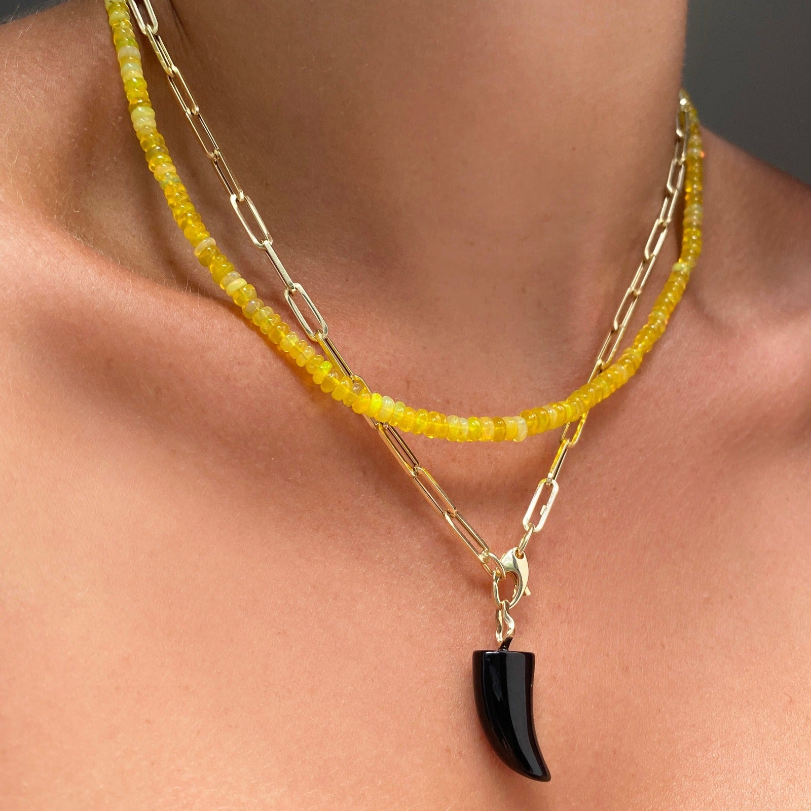Shimmering beaded necklace made of smooth opals in shades of yellow on a gold linking ovals clasp
Styled on a neck layered with a paperclip chain with a Black Horn Charm dangling