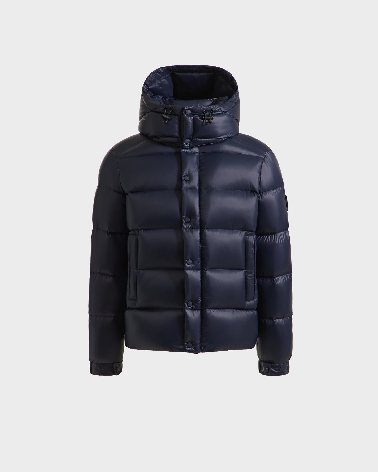 The Rudsak BRAYDEN S - M125525 Navy is a men's quilted down puffer jacket with a hood, front button closure, two large pockets, and adjustable drawstrings, shown against a plain white background.